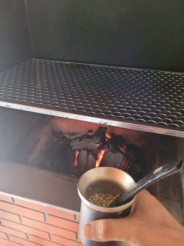 A gourd of tereré in hand, the grill behind it and the embers just starting