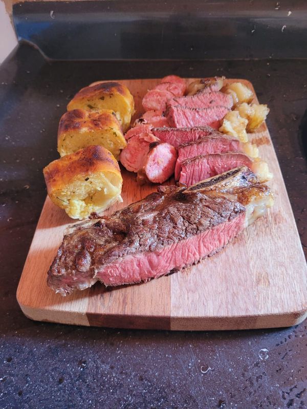 Sliced steak, rare, on a wooden board with garlic bread beside it