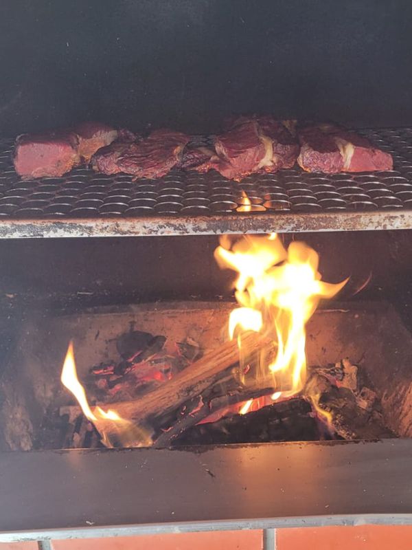Steaks on the grate with tall flames rising from the wood below