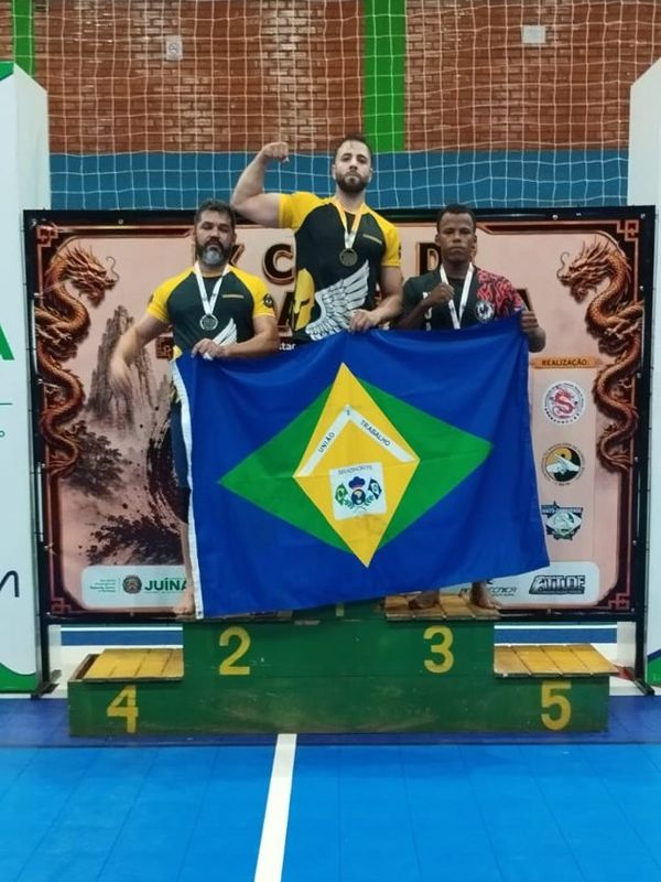Ed on a championship podium with teammates, holding the flag of Mato Grosso