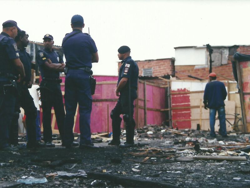 Police officers standing before shacks in a community